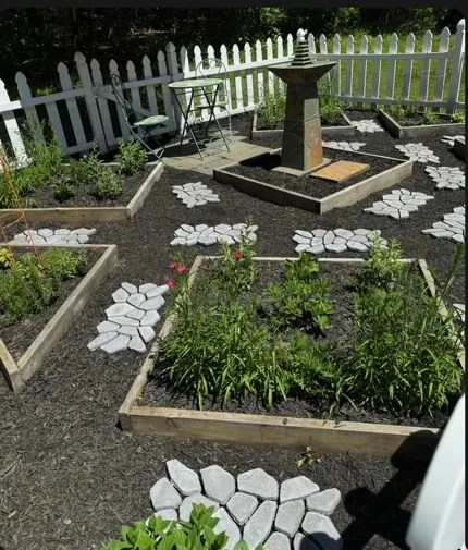 Raised garden beds with decorative stone paths and a central birdbath